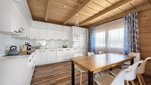 A modern kitchen with white cabinets, a wooden dining table, and a large window with curtains. - Tatra Wooden Apartment (Czarny Dunajec)