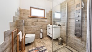Une salle de bain moderne avec un plancher en bois, une douche à parois de verre, des toilettes, un lavabo et une fenêtre.