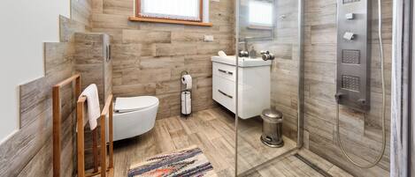 A modern bathroom with a wooden floor, a glass shower enclosure, a toilet, a sink, and a window.