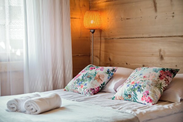 A neatly made bed with floral pillows, a rolled white towel, and a floor lamp with a woven shade. - Tatra Wooden Apartment (Czarny Dunajec)
