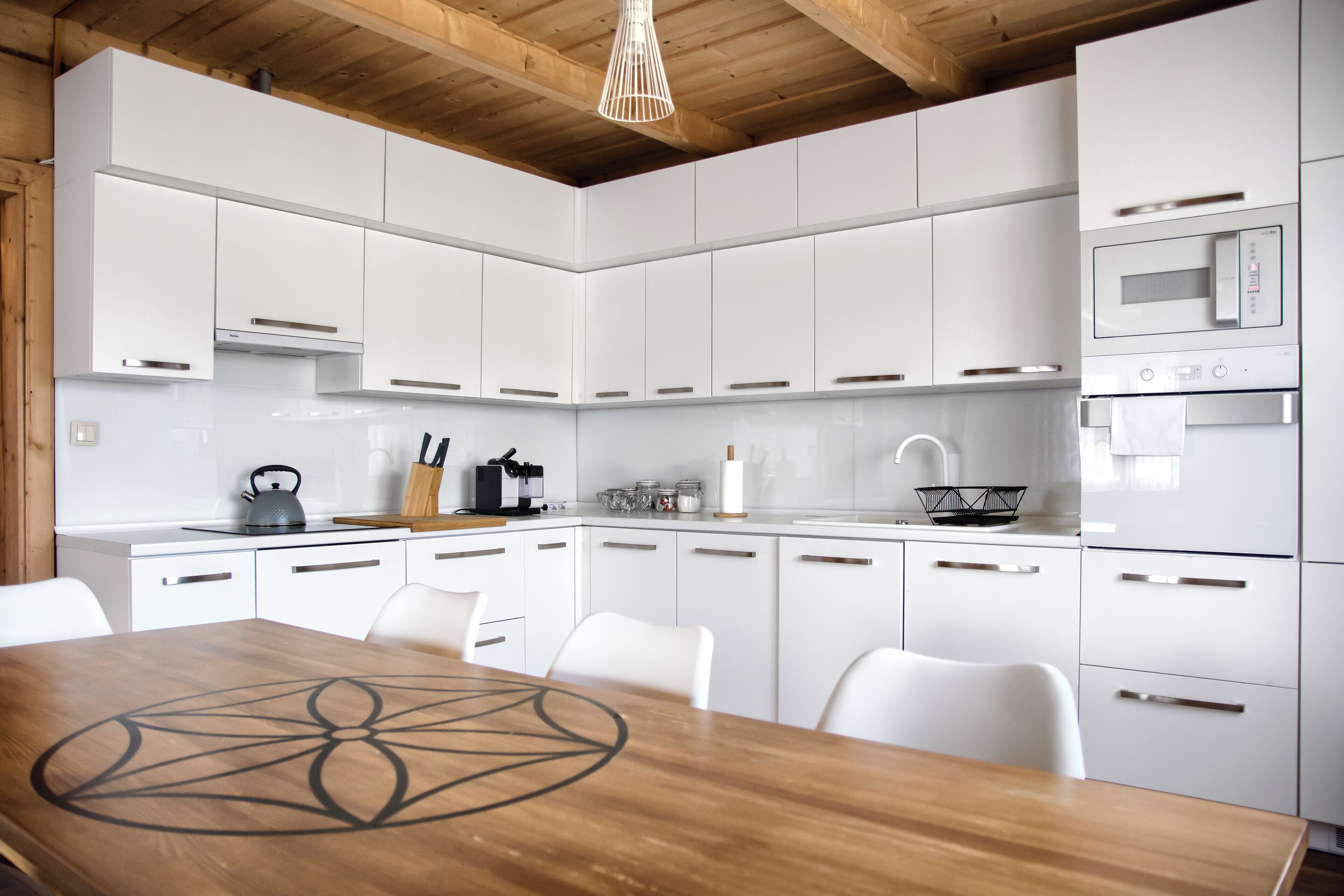 Een moderne keuken met witte kastjes, een houten eettafel en een hanglamp.