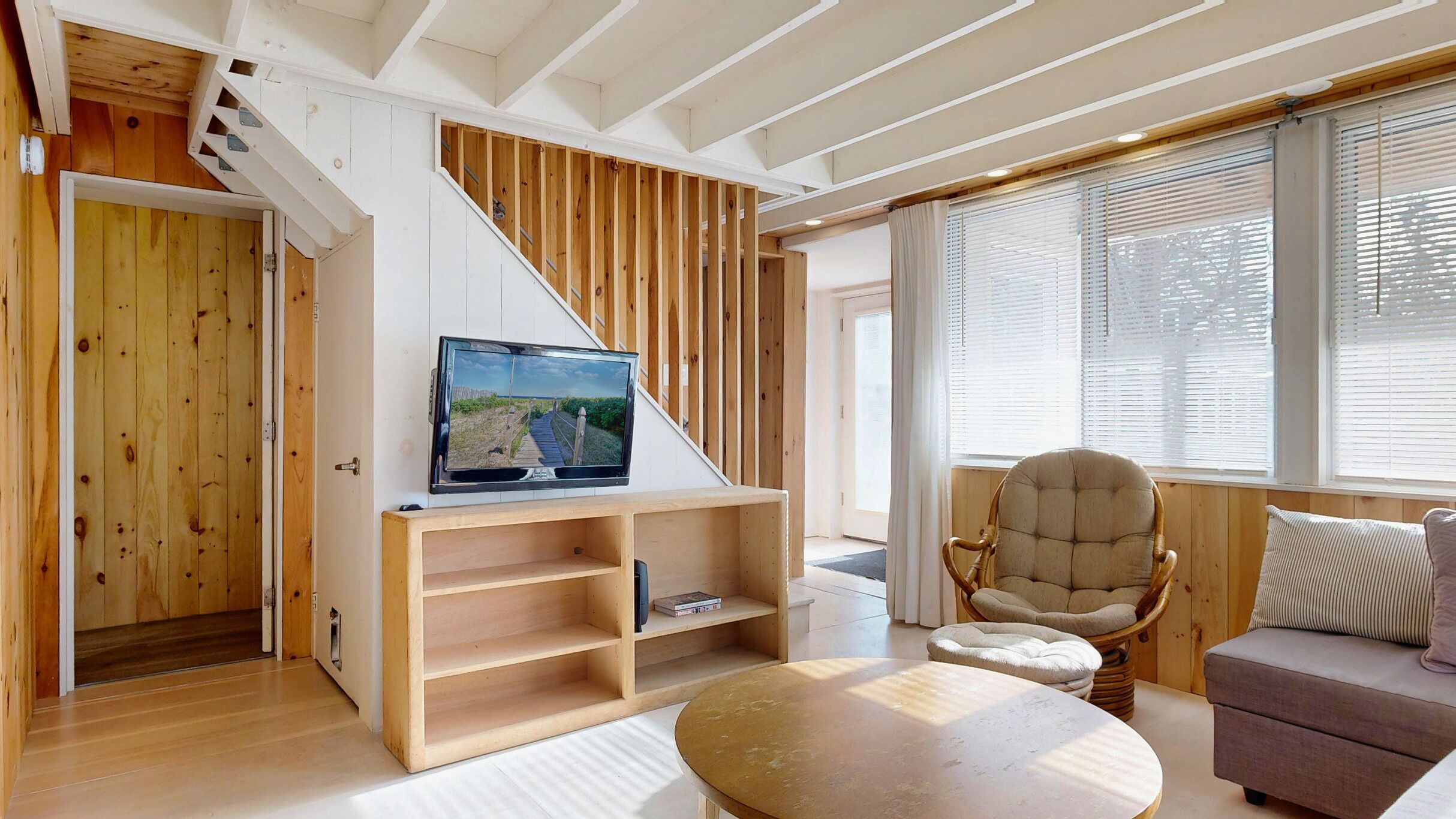 Una sala de estar moderna con una escalera de madera, un televisor sobre un estante de madera, un sillón de mimbre y un sofá.