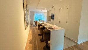 A modern kitchen with white cabinets, a central island with bar stools, and a dining area with a long table and chairs. - Apartment in Brussels Near European Parliament (Brussels)