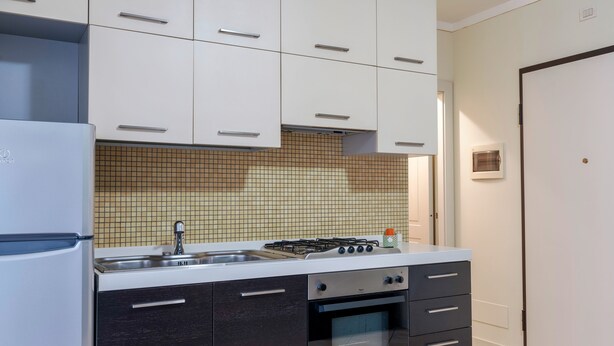 A compact kitchen with white upper cabinets, a gas stove, a built-in oven, and a sink. - FIORDALISi Apartment (Desenzano del Garda)