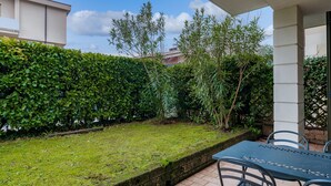 A patio area with a table and chairs, a neatly trimmed hedge, and a view of a building in the background. - FIORDALISi Apartment (Desenzano del Garda)