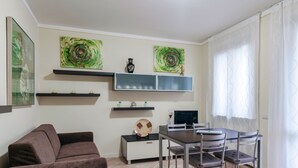 A modern living room with a brown sofa, a dining table with chairs, a TV, and abstract art on the walls. - FIORDALISi Apartment (Desenzano del Garda)