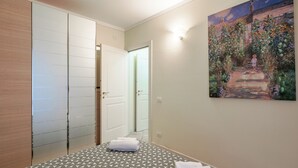 A hotel room with a geometric patterned floor, a painting of a garden on the wall, and a door leading to another room. - FIORDALISi Apartment (Desenzano del Garda)