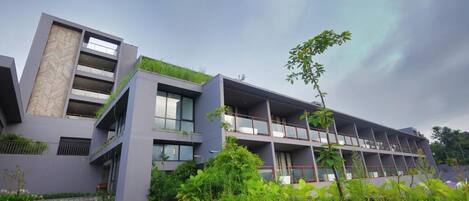 A modern building with multiple balconies, green roofs, and a stone staircase leading to the entrance.