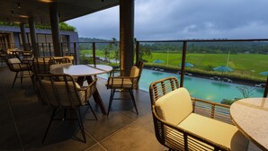 A restaurant with wicker chairs and tables, overlooking a swimming pool and lush green fields. - Saptha Resort and spa (Sulthan Bathery)