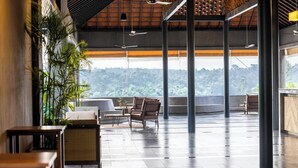 A spacious indoor area with a high ceiling, large windows offering a view of a forested landscape, and several seating areas with tables. - Saptha Resort and spa (Sulthan Bathery)