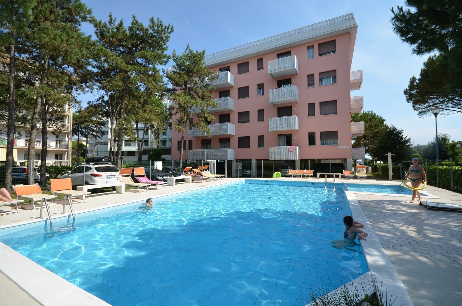 Una piscina con sillas de descanso y un edificio con balcones al fondo.