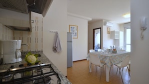 A kitchen with a gas stove, a coffee maker, and a dining area with a table and chairs. - Contemporary apartment in the heart of Lido del Sole (San Michele Al Tagliamento)