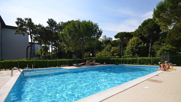 A rectangular swimming pool with clear blue water, surrounded by a paved deck. - Contemporary apartment in the heart of Lido del Sole (San Michele Al Tagliamento)
