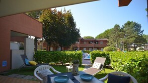 An outdoor patio area with a table set for two, surrounded by lounge chairs and a small garden. - Relaxing holiday apartment (Bibione)