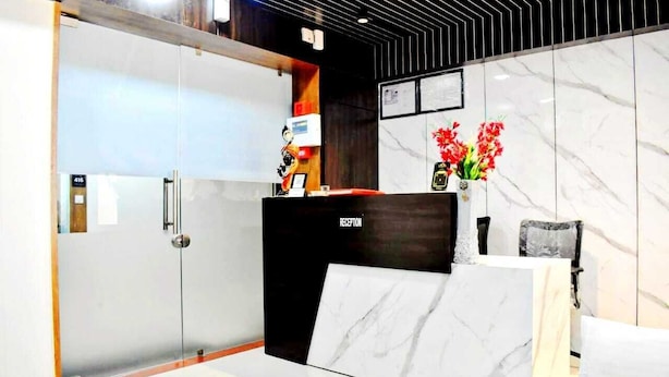 A reception area with a marble reception desk, a glass door, and a wall-mounted clock. - Hotel White House (Ahmedabad)