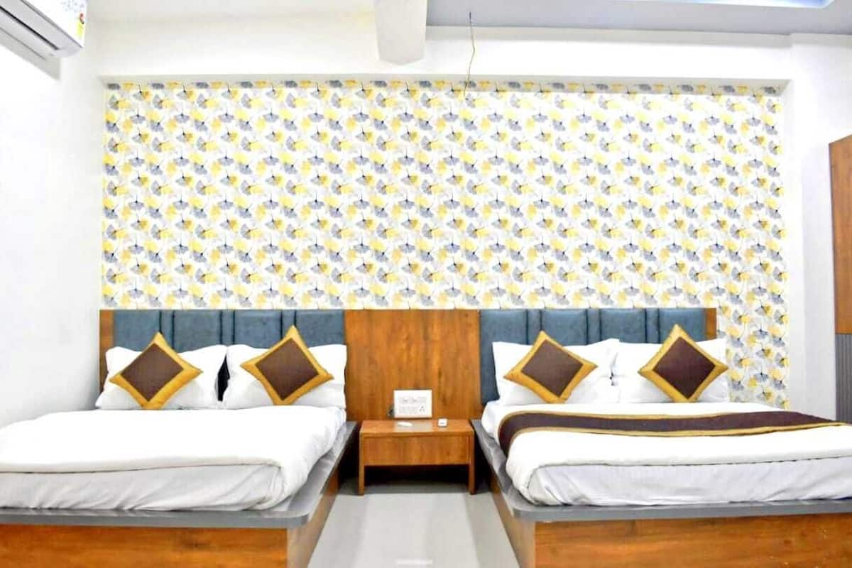 Une chambre double avec deux lits, une tête de lit en bois, un mur décoré d’un motif et une petite table de chevet avec une lampe.