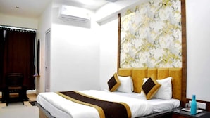 A hotel room with a bed, a nightstand, a chair, and a wall with a floral pattern. - Hotel White House (Ahmedabad)