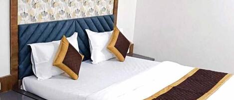 Ein ordentlich bezogenes Bett mit blauem Kopfteil und einem gemusterten Wandpapier darüber.
