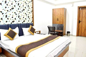 Quarto de hotel com cama, escrivaninha, cadeira, guarda-roupa e lixeira.