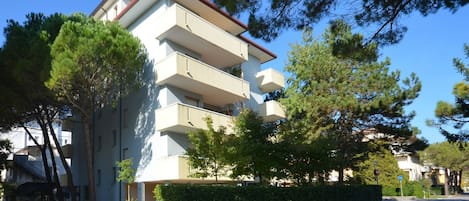 Un edificio residencial de varios pisos con balcones, rodeado de árboles y setos.