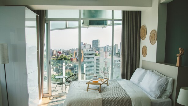 A modern hotel room with a large bed, a balcony with a view of the city, and a small table with a tray. - Chic Loft w/ AC, Walkable Area (Cuauhtémoc)