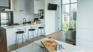 A modern kitchen with a central island, bar stools, a flat-screen TV, and a city view through large windows. - Chic Loft w/ AC, Walkable Area (Cuauhtémoc)