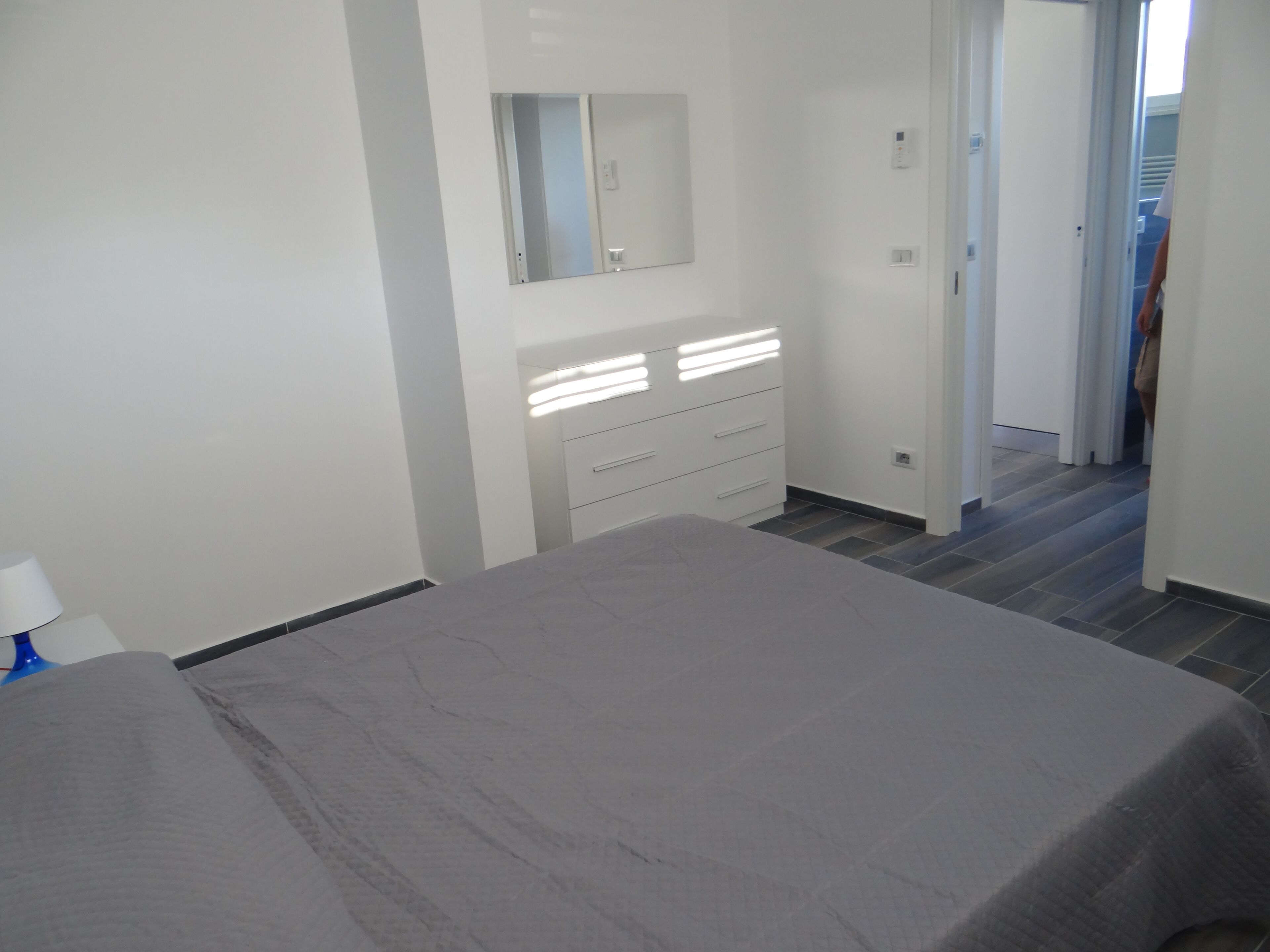 Ein Schlafzimmer mit Bett, Kommode, Spiegel und einer Tür zu einem Flur.