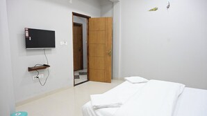 A bedroom with a bed, a TV mounted on the wall, a wooden wardrobe, and a door leading to another room. - Hotel RRR Palace (Maheshwar)