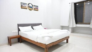 A neatly made bed with white linens in a modern room with a wooden headboard, a small bedside table, and a window with curtains. - Hotel RRR Palace (Maheshwar)