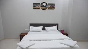 A neatly made bed with white linens, a dark headboard, and a nightstand with a pink mug. - Hotel RRR Palace (Maheshwar)