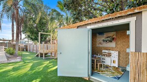 Una casita de juegos con techo de paja, tobogán y una pequeña cocina al aire libre con mesa y sillas.
