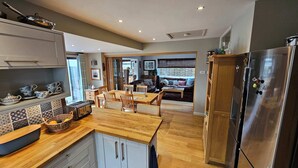 A modern kitchen with a dining area, wooden cabinets, a stainless steel refrigerator, and a view into the living room. - Couples retreat on Dartmoor with stunning views (Mary Tavy)
