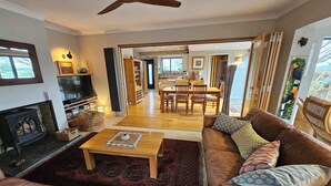 A living room with a fireplace, a television, a sofa, a coffee table, and a dining area with chairs and a table. - Couples retreat on Dartmoor with stunning views (Mary Tavy)