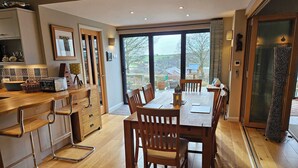 A modern kitchen with wooden cabinets, a dining table with chairs, and a large window offering a view of the outdoors. - Couples retreat on Dartmoor with stunning views (Mary Tavy)