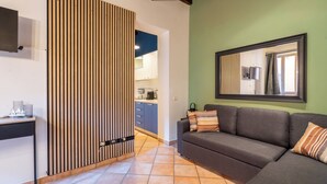 A living area with a sofa, a coffee table, a TV, and a kitchen in the background. - FREEDOM INDUSTRIAL CENTRALLY LOCATED FOR FAMILIES AND WORKERS (Parma)