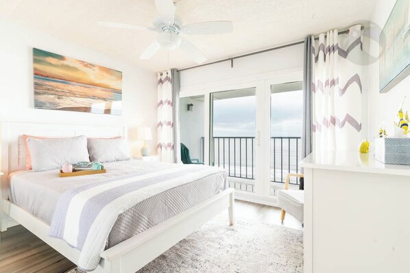 A bedroom with a bed, a ceiling fan, a view of the outdoors, and a balcony.