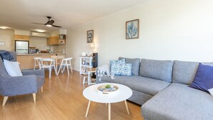 A modern living room with a grey sofa, a white coffee table, and a dining area with a kitchen in the background. - The Marina 308 - central Forster (Forster)