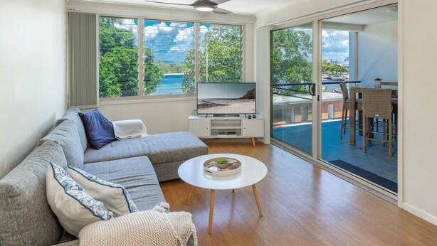 A modern living room with a large TV, a sofa, a coffee table, and a balcony with outdoor seating. - The Marina 308 - central Forster (Forster)