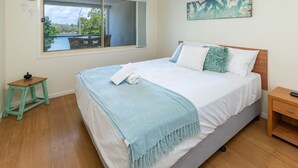 A bedroom with a bed, a small table, a nightstand, a window with a view of a body of water, and a painting on the wall. - The Marina 308 - central Forster (Forster)
