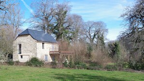 A stone house with a sloped roof, surrounded by trees and a grassy field. - A small house above the meadows. Light, space and silence. (Rieupeyroux)