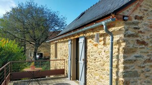 A stone building with a wooden deck and a metal railing. - A small house above the meadows. Light, space and silence. (Rieupeyroux)