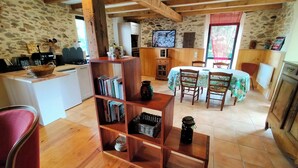 A cozy, rustic interior with a wooden bookshelf, a dining table with chairs, a kitchen area, and a television. - A small house above the meadows. Light, space and silence. (Rieupeyroux)