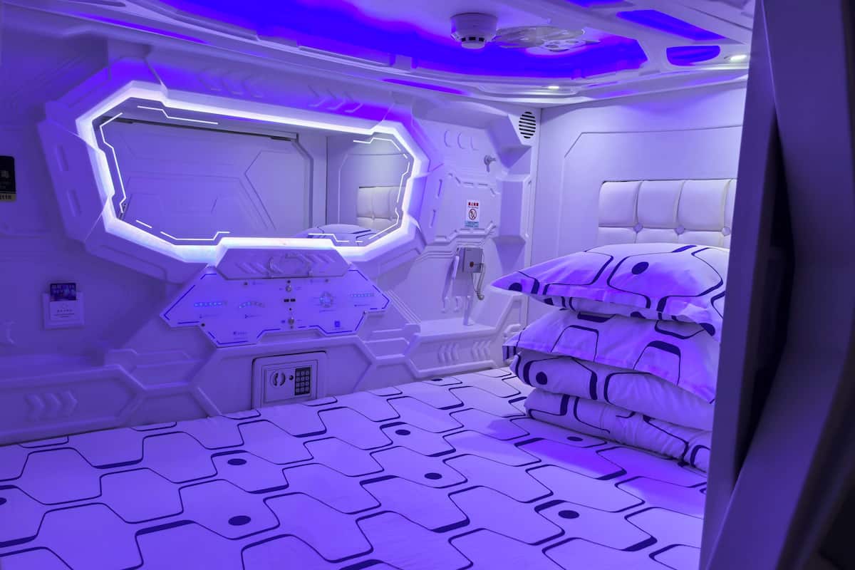 Ein futuristisches Zimmer mit einem geometrischen Bodenmuster, einer zentralen Bedienkonsole und einem Bett mit gemusterten Kissen.