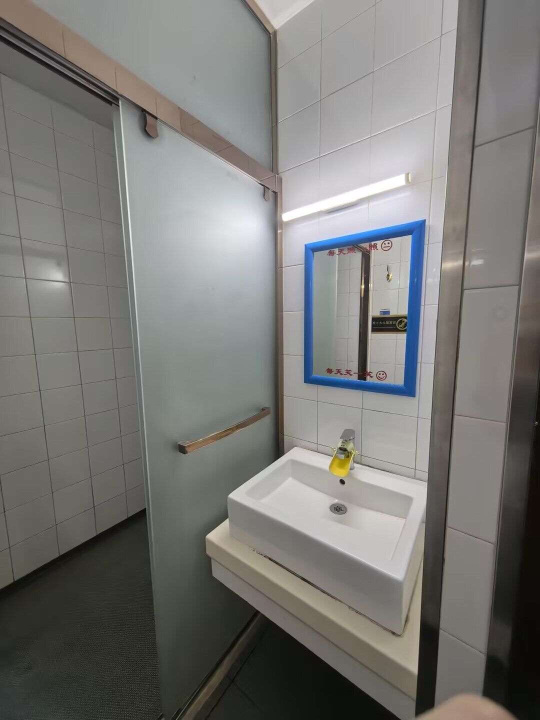 Un baño con un lavamanos blanco, un espejo con marco azul y una barandilla.