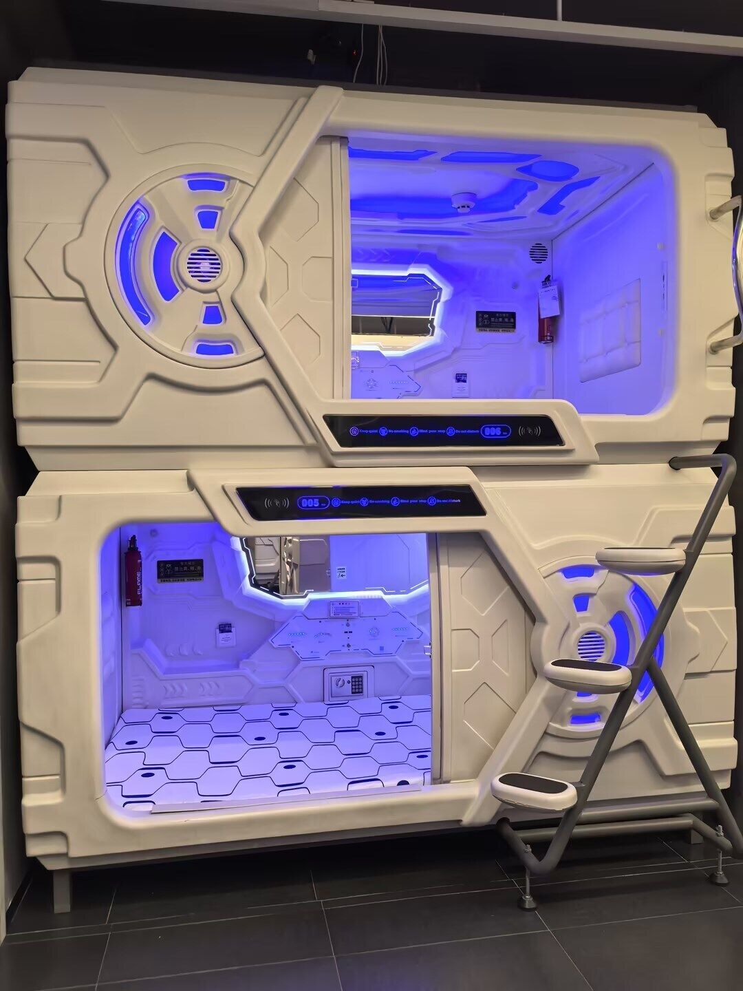 Une pièce futuriste avec un motif hexagonal sur le sol, un panneau de contrôle et une échelle.