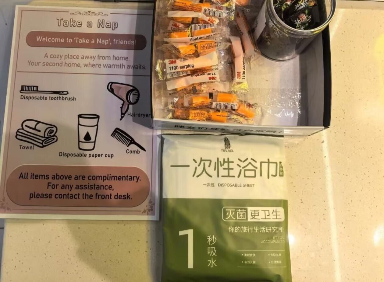 A hotel room with a welcome sign, a box of toiletries, a disposable paper cup, and a disposable sheet.