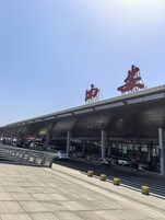 Terminal de aeropuerto con un gran cartel rojo, pasillo cubierto y coches estacionados.