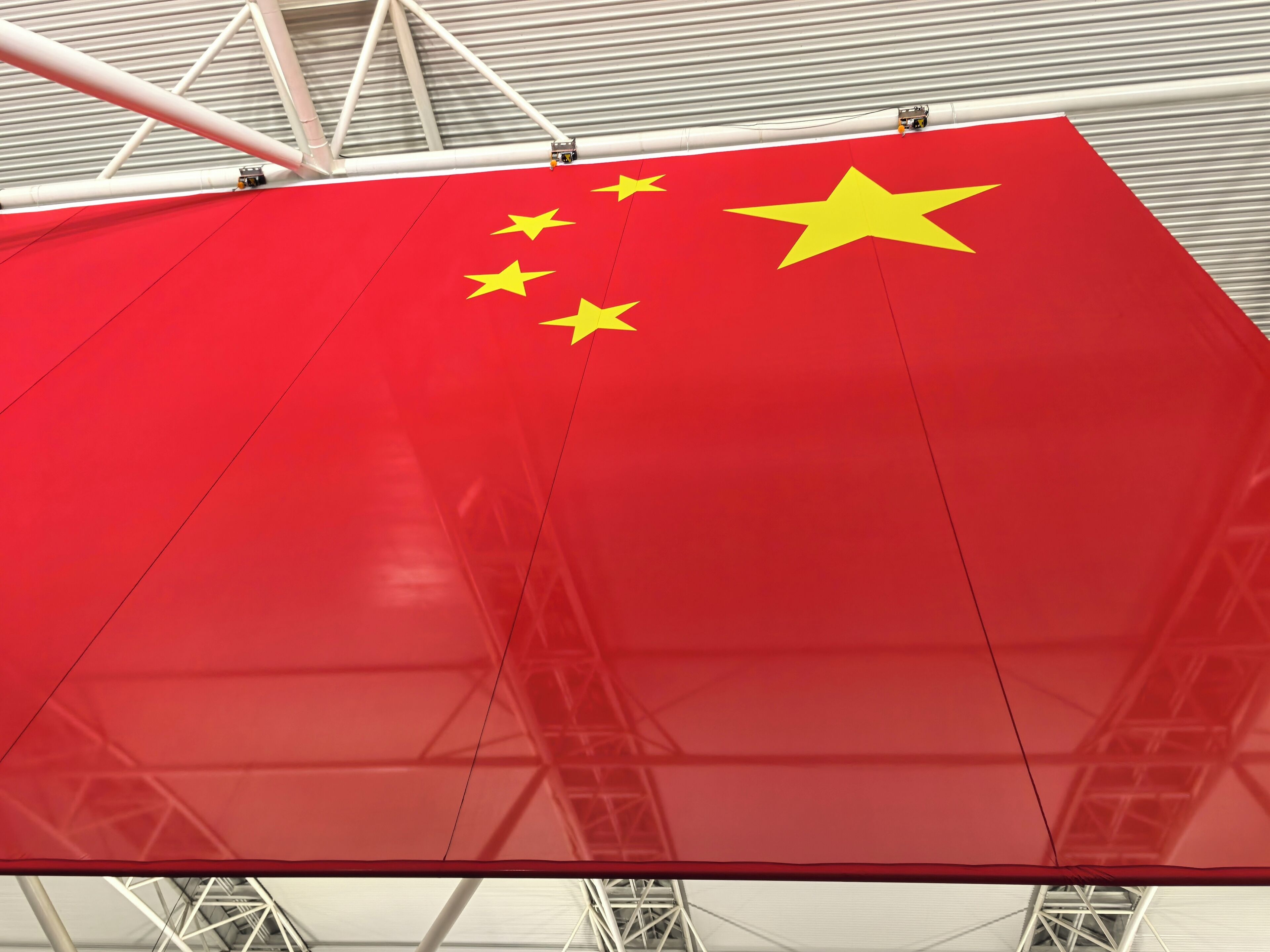 Un grand drapeau rouge orné d’étoiles jaunes et d’un emblème en forme d’étoile, fixé sur une structure métallique.