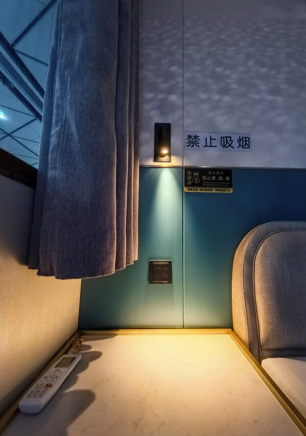 A train compartment with a blue wall, a curtain, a sign prohibiting smoking, and a remote control on the floor.