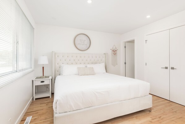 A bedroom with a large bed, a bedside table with a lamp, a wall-mounted artwork, and a wardrobe.